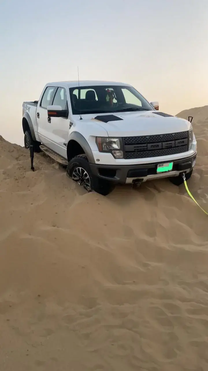 White pickup truck sunk into soft sand on a dune with a yellow recovery strap lying on the sand beside it