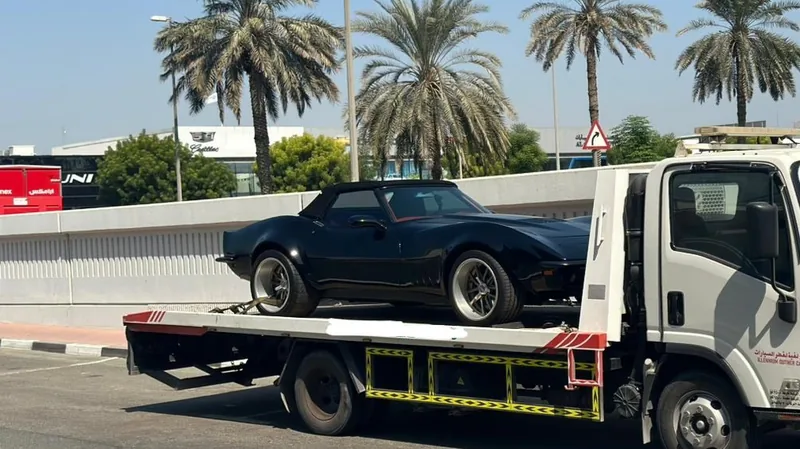 Black classic Chevrolet Corvette Stingray loaded onto Millennium recovery flatbed truck near Cadillac Dubai showroom on Sheikh Zayed Road